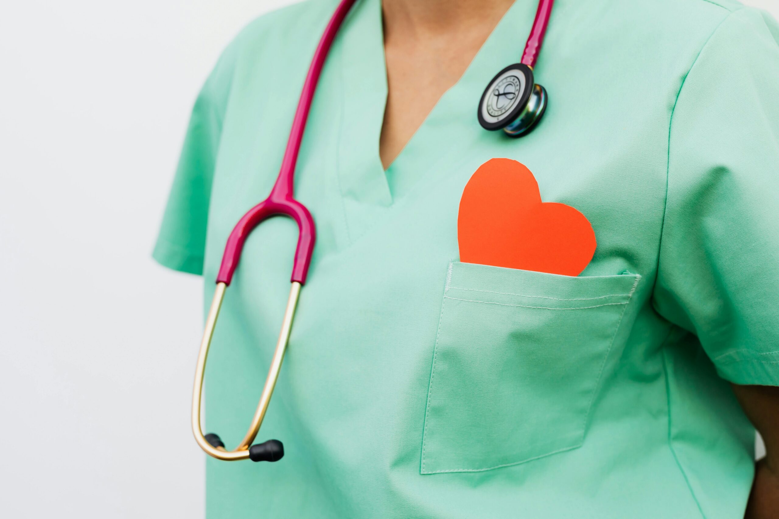 Nurse's torso with a stethoscope around their neck and a red paper heart in their pocket